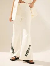 Pantalón Oxford color blanco con apliques bordados en hilo y piedras brillantes en la parte inferior de la bota.