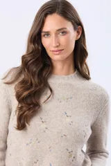 Buzo tejido de punto en color beige, con cuello redondo, mangas largas y puños acanalados. Presenta un delicado diseño bordado con motivos florales dispersos en el frente y una etiqueta de cuero sintético en el ruedo.