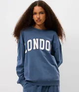 Buzo cerrado de fleece color azul, con cuello redondo, mangas largas, puños y ruedo ajustados. Presenta estampa frontal con la palabra "LONDON" en letras blancas con borde oscuro.