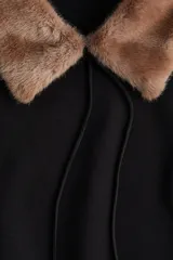 Buzo negro de felpa con interior suave, cuello de piel sintética en color marrón, mangas largas con hombros caídos y puños y bajo acanalados. Presenta tiras finas para atar en el frente.