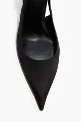Zapatos de tacón tipo slingback con punta fina, confeccionados en satén negro. Presentan una tira ajustable en el talón con hebilla metálica lateral y tacón fino.