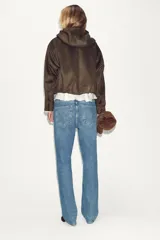 Chaqueta bomber de efecto ante en color marrón, con capucha ajustable mediante cordones, cierre frontal con cremallera, bolsillos laterales y bajo con elástico interior.