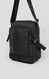 Bolso cruzado (bandolera) negro de tela sintética, con correa ajustable estampada con la palabra "LUXO". Presenta un diseño estructurado con bolsillo frontal y parche con logo en la base.