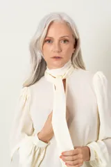 Blusa color marfil de manga larga con frunce en hombros y puños, escote en V con lazo y cierre de puños con dos botones.