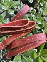 Llavero de cuero en formato de tira con diseño minimalista, confeccionado en cuero genuino marrón con interior en contraste color fucsia, pespuntes rosados y herrajes metálicos envejecidos con gancho tipo mosquetón.