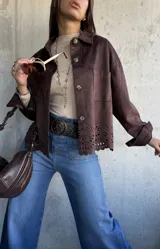 Chaqueta de gamuza color chocolate, con corte recto, cuello clásico y cierre frontal con botones. Presenta un diseño calado decorativo en el ruedo y bolsillos frontales tipo parche.