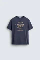 Camiseta de corte relajado, color azul marino, con cuello redondo y manga corta. Presenta un estampado frontal con texto y diseño en tono dorado con efecto desgastado.