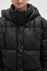 Campera puffer color beige con diseño capitoneado, capucha integrada y cierre frontal oculto. Presenta bolsillos laterales y un corte holgado.