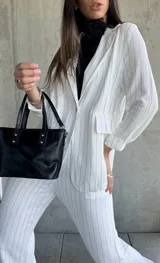 Blazer blanco con finas rayas verticales negras, solapas clásicas, cierre con un botón y bolsillos frontales.