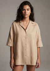 Camisa negra de manga corta con cuello tipo solapa y botones frontales. Presenta bordados sutiles en tono negro en las mangas y en la parte inferior delantera.