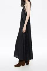 Vestido largo negro con caída fluida, escote en V con tirantes finos y detalles de encaje floral en el escote y el pecho.