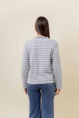 Remera de manga larga con diseño de rayas horizontales verdes sobre fondo crudo, cuello redondo con detalle de volado y cartera frontal con botones.