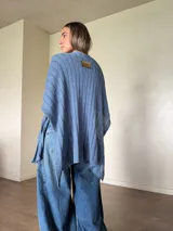 Ruana tejida de algodón con hilo lurex en punto jersey, color azul, con diseño amplio y detalle de etiqueta de cuerina en la parte posterior.