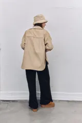 Camisa de pana color beige, con corte oversize, cuello clásico, bolsillos frontales y cierre con botones.