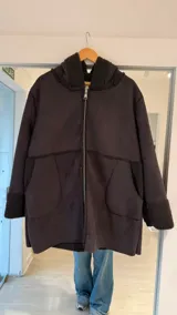 Tapado tipo campera de gamuza sintética color gris oscuro, con interior y detalles en corderito negro. Presenta cierre frontal, capucha y bolsillos laterales.