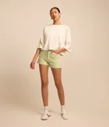 Short de sarga color blanco, de cintura alta, con bolsillos delanteros y traseros, trabillas para cinturón y bajo plegado. Cuenta con cierre frontal de botón y cremallera.