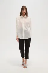 Camisa blanca de poliéster, de corte ancho y manga larga, con cuello redondo y apliques de strass y tachas distribuidos por toda la prenda.