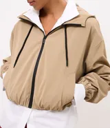 Campera cortaviento Marfinno de color beige, diseño corto con capucha, cierre frontal de cremallera con tiradores negros, bolsillos laterales y elástico fruncido en el ruedo y los puños.