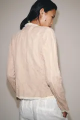 Chaqueta de punto color rosado con cuello redondo, manga larga y bolsillos delanteros. Presenta detalles de acabados con tejido combinado deshilachado en color blanco crudo y cierre frontal con lazos del mismo tono.