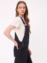 Mono de jean negro con diseño de jardinera, de corte recto y holgado, con bolsillos frontales y laterales.