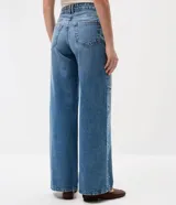 Pantalón wide leg de tiro bajo confeccionado en jean de algodón, con diseño amplio y aplicación de tachas y ojalillos metálicos a lo largo de los laterales.