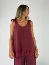 Top de viscosa color bordó, con escote redondo, tirantes ajustables con lazos en los hombros y detalle de volados en el ruedo.