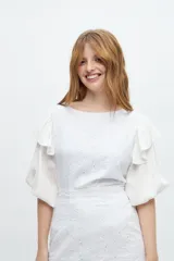 Blusa blanca con bordado calado, mangas abullonadas y volados en los hombros.