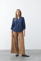 Camisa negra de corte clásico con escote en V, botones frontales y mangas largas con puños. Presenta detalles de recortes calados en la zona de los hombros.