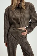 Blazer corta de corte recto con estampado de cuadros pequeños en tonos marrones y negros. Presenta cuello solapa, manga larga y cierre frontal con un botón.