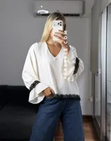 Blusa de tela cey color bordó, con escote en V y mangas largas abullonadas que terminan en puños con detalle de encaje y volados.