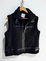 Chaleco estilo gamulán con interior y bordes de corderito sintético. Presenta cierre frontal, cuello solapa con hebillas decorativas y bolsillos laterales.