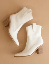 Bota texana de caña media color blanco, con taco cuadrado de madera y punta ligeramente afinada. Presenta un diseño minimalista con cierre posterior y tiradores laterales.