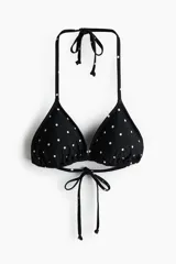 Top de bikini triangular negro con estampado de lunares blancos, copas con relleno extraíble y tiras para anudar al cuello y la espalda.