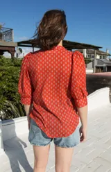 Camisa de estilo romántico color rojo con estampado floral pequeño en tono azulado, cuello redondo, cierre frontal con botones y mangas al codo con frunces en los hombros.