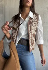 Chaleco de color beige con bordados decorativos en color crema en los paneles frontales. Presenta un diseño sin mangas con corte recto y terminaciones limpias.