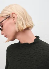 Top de crepé con textura, color verde oscuro, diseño entallado, cuello festoneado y manga larga.