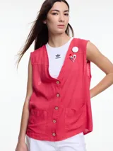 Chaleco sin mangas color coral, con escote en V, cierre frontal con botones de madera y bolsillos de parche. Incluye tres pins decorativos: un corazón plateado, un círculo plateado y un cuadrado rojo. Confeccionado en tejido liviano de lino y viscosa.