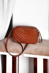 Cartera bandolera negra con diseño capitoneado en forma de V, correa de cuero y cadena plateada, cierre metálico y doble bolsillo interior.