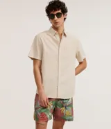 Bermuda de baño para hombre, color base rojizo/terracota, con estampado tropical de hojas verdes y bananas. Posee cintura elástica con cordón ajustable y bolsillos laterales.