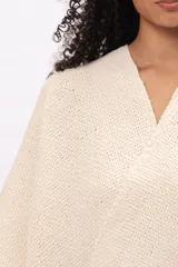 Ruana de tejido de punto en color crudo, con diseño abierto, flecos en el borde inferior y etiqueta de cuero con la marca Pura Lana en el frente.