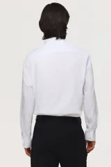 Camisa blanca de manga larga con cuello inglés, tapeta lisa y bajo redondeado. Presenta canesú en la espalda y puños ajustables con botón.