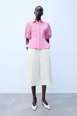 Camisa de popelín a rayas rosadas y blancas, con cuello solapa, mangas abullonadas por debajo del codo con terminación elástica, cintura entallada y bajo en evasé. Cierre frontal con botones ocultos.