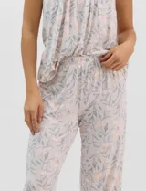 Pijama compuesto por remera sin mangas con escote redondo, botones frontales y detalle de puntilla, acompañado de un pantalón capri con cintura elástica. Presenta un estampado floral en tonos rosados sobre base gris.
