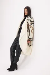 Spolverino largo de tejido de punto en color crudo, con diseño de patrones geométricos en tonos marrón y negro. Presenta un corte abierto con solapas amplias y mangas largas.