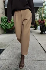 Pantalón de tiro medio con pinzas delanteras, bolsillos laterales y falsos bolsillos de vivo en la parte trasera. Presenta un corte holgado que se estrecha hacia el tobillo, con bajo acabado en pliegues y cierre frontal con cremallera, botón interior y gancho.