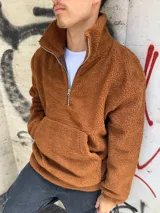 Buzo de corderito color marrón, con cuello alto y cierre frontal parcial. Presenta un bolsillo tipo canguro frontal y diseño holgado.