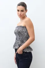 Top strapless (sin tirantes) de mujer, ajustado al cuerpo con efecto fruncido (smock) en todo el torso y un pequeño volante en el ruedo inferior. Presenta un estampado de cebra en blanco y negro.