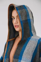 Ruana confeccionada en paño italiano con diseño a cuadros en tonos gris, azul y negro, con terminaciones ribeteadas en cuerina color camel y botón en las mangas.