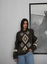 Sweater de punto marrón oscuro, tejido a mano con diseño geométrico y rombos en tonos beige y blanco, con cuello redondo y mangas largas.
