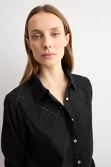 Camisa blanca de manga larga con frente de tela broderie con diseño de rombos calados y espalda lisa. Presenta cuello clásico y cierre frontal con botones.